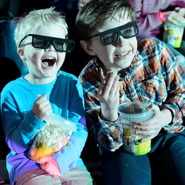 Children smiling and eating popcorn while watching a 4D movie at LEGO Studios 4D