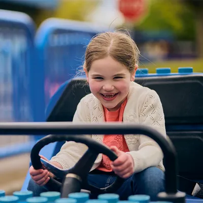 Girl in blue car smiling at LEGO City Driving School