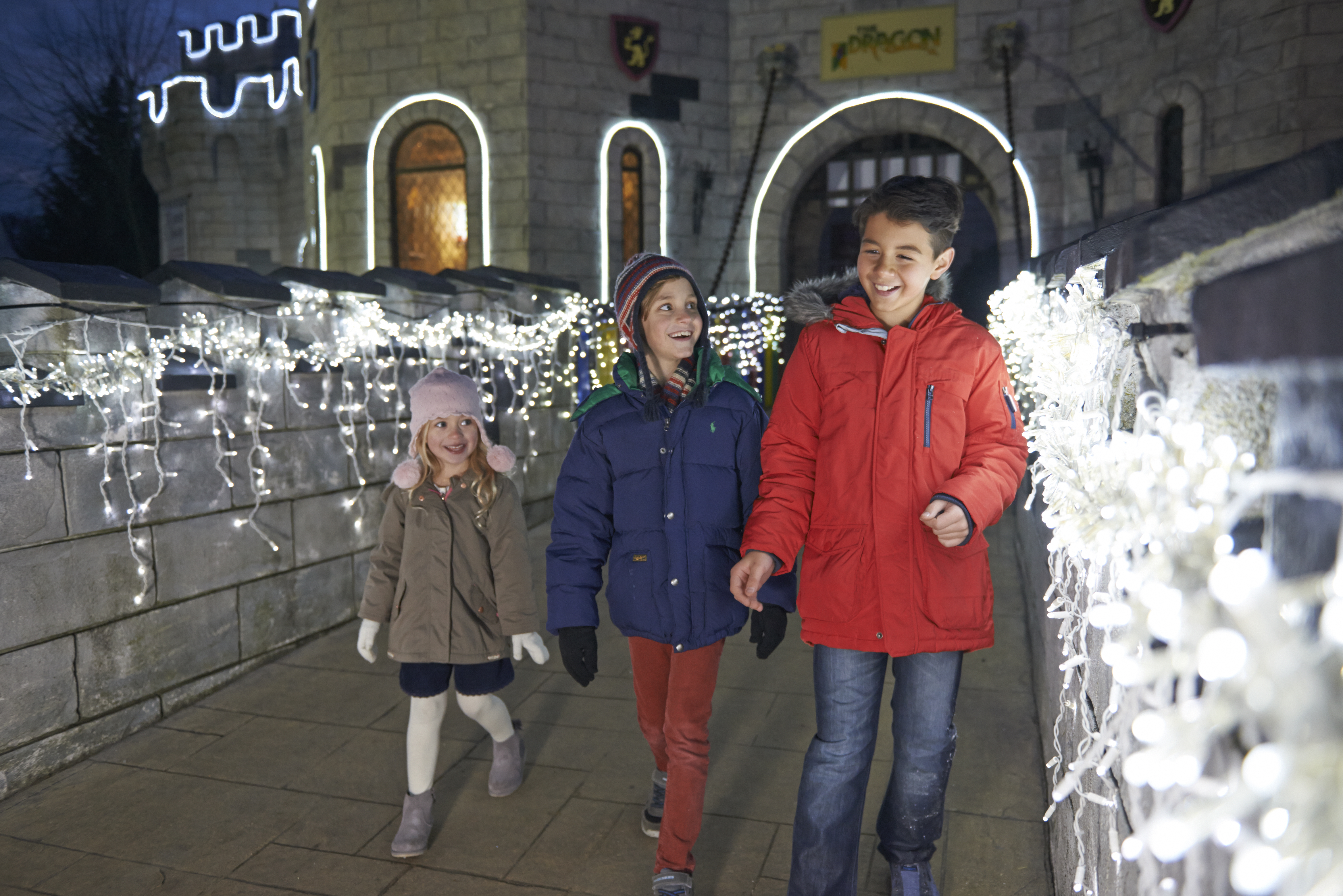Children crossing drawbridge of lit up castle at LEGOLAND at Christmas