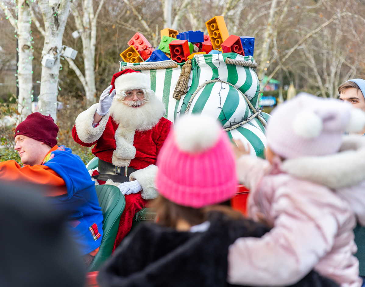 Father Christmas on a Sleigh waving, to a young woman and young girl both in pink hats 